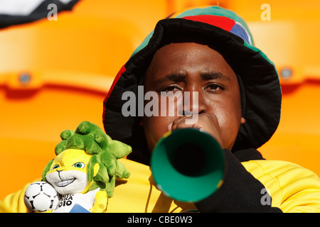 Un jeune ventilateur souffle une vuvuzela en maintenant un jouet mascot au match d'ouverture de la Coupe du Monde entre l'Afrique du Sud et le Mexique. Banque D'Images