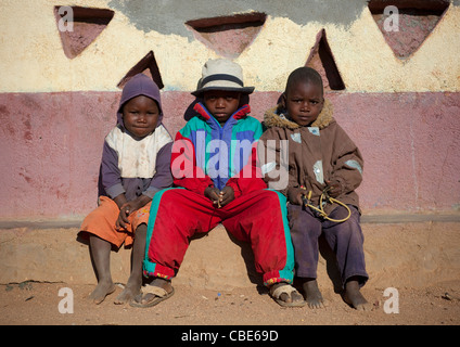 Enfants Himba habillée d'une manière occidentale assise sur un banc, Village d'Oncocua, Angola Banque D'Images