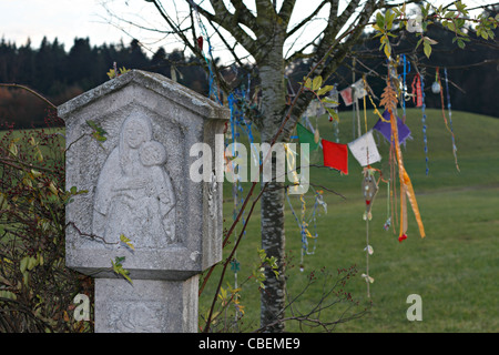 Marie Chistian Wayside culte avec les drapeaux de prière bouddhiste suspendu à des branches d'arbre, Chiemgau Haute-bavière Allemagne Banque D'Images