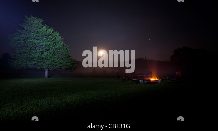 Chaises vides autour d'un foyer de nuit, avec la Lune se levant à l'arrière-plan sur un champ de Misty. Près de Deerfield, Virginia. Banque D'Images