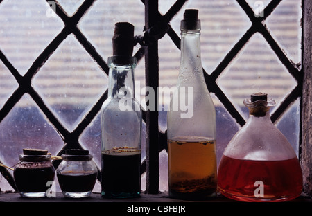 Collection de meubles anciens pots et bouteilles contenant des liquides colorés et debout sur rebord de fenêtre au plomb de diamants Banque D'Images