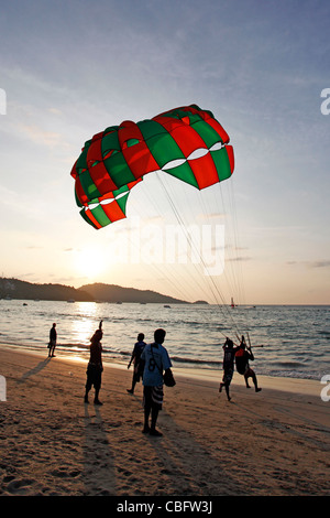 Les gens en silhouette au coucher du soleil avec un parachute Le parachute ascensionnel, l'une des activités sportives sur la plage de Patong, Patong, Phuket Banque D'Images