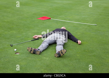 Un golfeur affolé allongé sur un green avec balle au bord du trou Banque D'Images