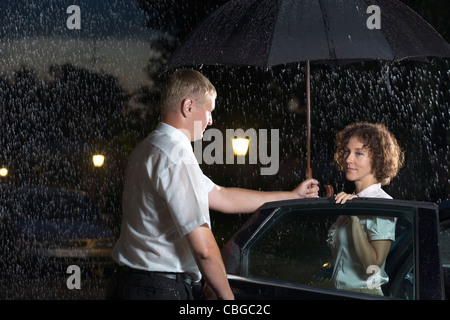 Un homme d'ouvrir votre porte et tenant un parapluie sur une femme Banque D'Images