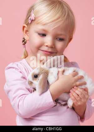 Portrait d'une fillette de trois ans tenant un lapin animal isolé sur fond rose Banque D'Images