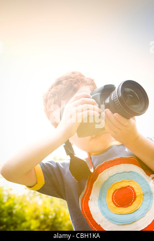 Un jeune garçon, âgé de 7 ans, en utilisant un appareil photo reflex numérique dans un jardin ensoleillé. Banque D'Images