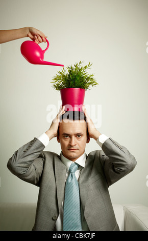 Photo de l'homme graves avec des plantes sur tête étant arrosé de pot d'arrosage Banque D'Images