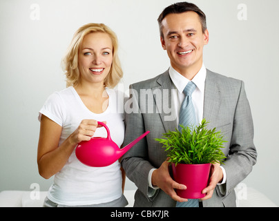 Photo de l'homme heureux avec plante et woman holding watering pot looking at camera Banque D'Images