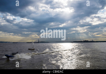 Le port de New York en fin d'après-midi sous un ciel couvert avec Statue de la Liberté et Ellis Island qui se profile au loin. Banque D'Images