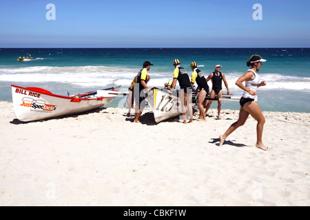 Surfez sur la concurrence des bateaux et une femme Surf Life Saver fonctionnant sur Scarborough Beach et l'Océan Indien, Perth Western Australia Banque D'Images