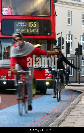 Deux cyclistes de signalisation tournez à gauche tout en voyageant le long d'un cycle superhighway à Londres, avec un bus rouge derrière Banque D'Images