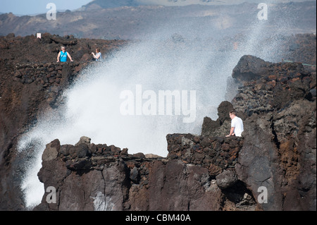 Touristes visitant Los Hervideros (les Boiling One), attraction touristique naturelle sur la côte où les coulées de lave du volcan solidifié ont été érodées par l'océan Atlantique entraînant wave.induced geysers, déversements et brume, Lanzarote, îles Canaries, Espagne. Banque D'Images