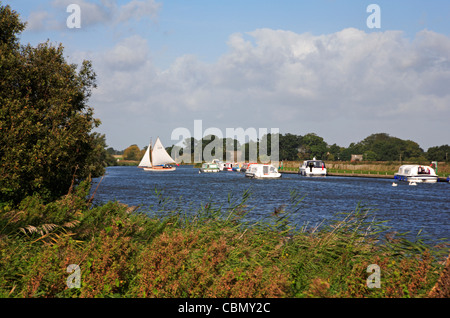 Une vue de vedette à moteur et un voilier virant sur la rivière Bure près de St Benet's Abbey, Norfolk, Angleterre, Royaume-Uni. Banque D'Images