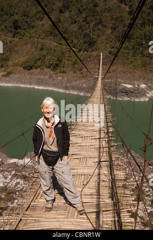 L'Inde, de l'Arunachal Pradesh, Kabang, contreforts de l'Himalaya, femme occidentale traversant pont suspendu au-dessus de la rivière Siang Banque D'Images