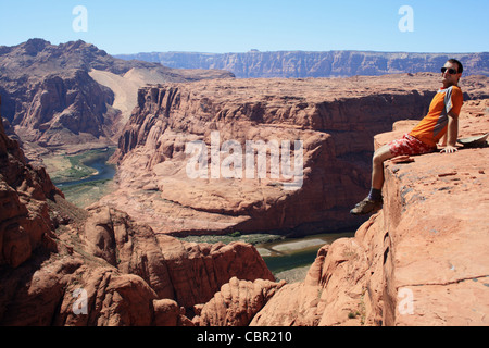 Image horizontale d'un homme assis sur le bord d'une falaise de grès surplombant Glen Canyon, Arizona Banque D'Images