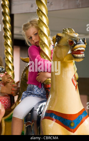 Close up portrait of vertical d'une petite fille s'accrocher à un cheval sur un carrousel manège à un champ de foire. Banque D'Images