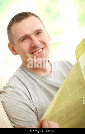 Hansome man reading newspaper, assis sur la table à la maison et souriant Banque D'Images