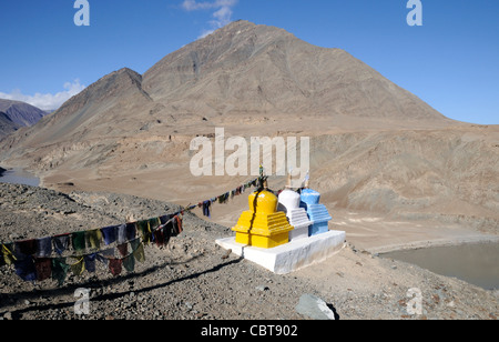 Drapeaux de prière et trois chortens couleur ou stupas marquer le confluent de la rivière Zanskar et l'Indus près de Nimu. Banque D'Images