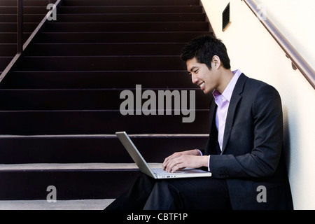 Asian businessman sitting on steps using laptop Banque D'Images