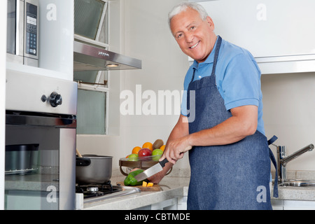 Portrait of happy senior man cutting vegetables au comptoir de la cuisine à la maison Banque D'Images