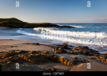 Les vagues roulent sur la plage tandis que la lumière du matin jette des ombres profondes dans les rochers sur la côte de Californie. Banque D'Images