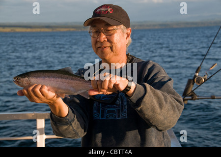 Un pêcheur tient fièrement sa truite arc-en-ciel qui a été pris sur un petit appât pour pêcher le Lac Taupo sur l'île du nord de la Nouvelle-Zélande Banque D'Images