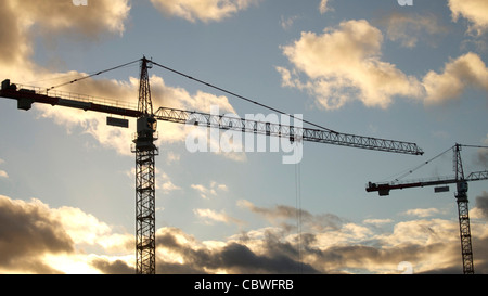 Grues de construction silhouettées contre un coucher de soleil avec des nuages visibles en arrière-plan Banque D'Images