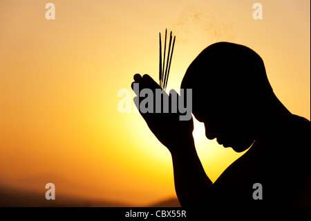 Priant avec encens indien au coucher du soleil. Silhouette. L'Inde Banque D'Images