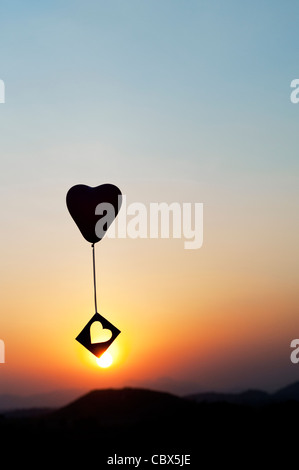 Avec ballon coeur découper des forme de coeur à la dérive dans un ciel de coucher du soleil. Silhouette Banque D'Images