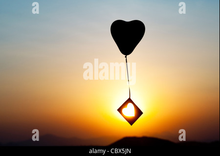 Avec ballon coeur découper des forme de coeur à la dérive dans un ciel de coucher du soleil. Silhouette Banque D'Images