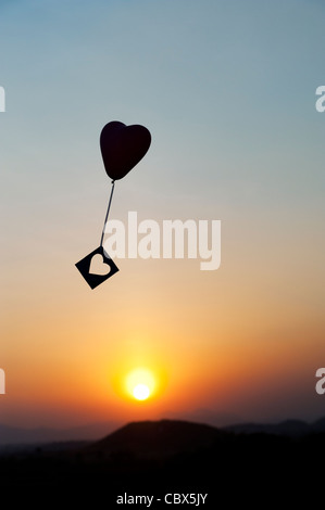 Avec ballon coeur découper des forme de coeur à la dérive dans un ciel de coucher du soleil. Silhouette Banque D'Images