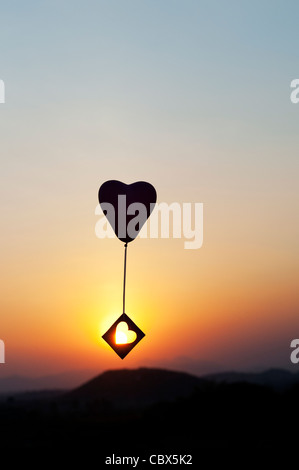 Avec ballon coeur découper des forme de coeur à la dérive dans un ciel de coucher du soleil. Silhouette Banque D'Images