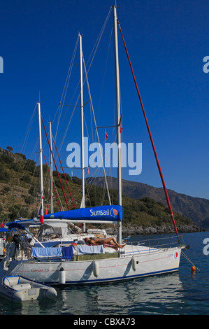 Location de bateaux à voile dans la baie de Karacaoren, Turquie, côte lycienne. Une belle jeune femme est couché sur la plate-forme elle-même de bronzage. Banque D'Images