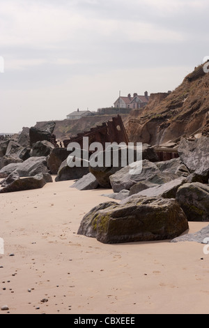 Littoral Happisburgh, North Norfolk, l'East Anglia. L'érosion des falaises de la mer du Nord ; les maisons, à côté du rendez-vous. Les roches importées de pouvoir atténuer les vagues. Banque D'Images