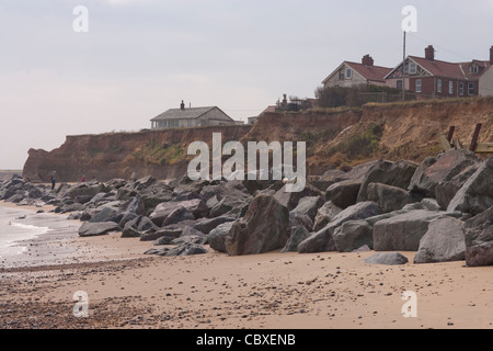 Littoral Happisburgh, North Norfolk, l'East Anglia. L'érosion des falaises de la mer du Nord ; des maisons sur falaise, roches importées ci-dessous. Banque D'Images