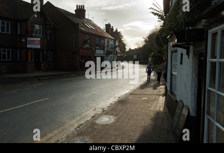 Deux personnes marchant le long d'un trottoir dans une scène de rue haute vide Chalfont St Peter Bucks UK centre village Banque D'Images