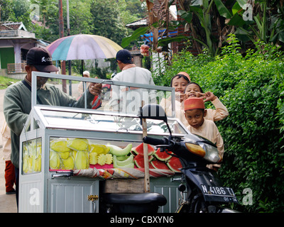 Les enfants de l'école se réunir autour d'un vendeur de rue, la vente de fruits frais au village rural à Java en Indonésie Banque D'Images