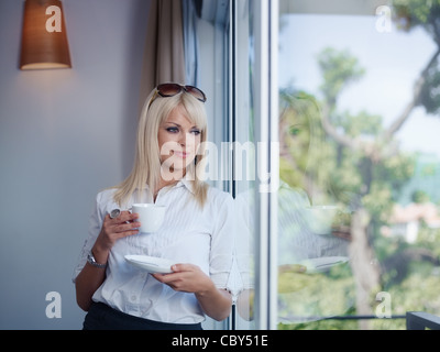 Mid adult businesswoman relaxing et boire une tasse de thé, regarder par la fenêtre. Jusqu'à la taille, vue avant, copy space Banque D'Images