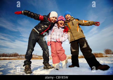 Enfants joyeux dans winterwear looking at camera tout en ayant des temps heureux à l'extérieur Banque D'Images