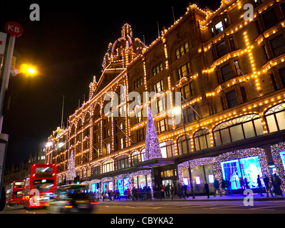 LONDON Shopping de Noël du magasin Harrods au crépuscule avec des lumières de Noël shoppers et passant les taxis et bus rouge Knightsbridge Londres SW1 Banque D'Images