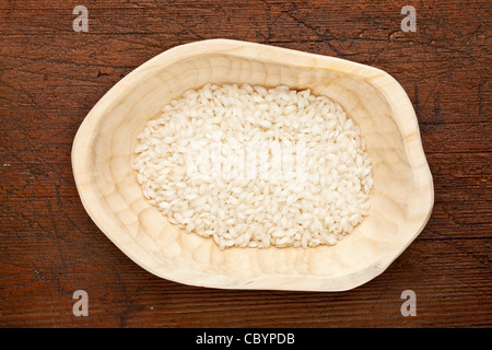 Grain de riz arborio, utilisé pour les repas traditionnels italiens, risotto, dans un bol en bois rustique contre la surface de la table en bois sombre grunge Banque D'Images