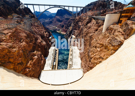 À la recherche vers le bas à partir du dessus de l'immense mur de béton du barrage Hoover. Sur la droite se trouve le centre des visiteurs. Tout en haut du cadre est le Mike O'Callaghan - Pat Tillman Memorial Bridge. Au milieu est l'écoulement de la rivière Colorado, avec les deux bâtiments abritant les turbines hydroélectriques sur chaque côté de la rivière. Le barrage s'étend sur la frontière de l'état, avec à gauche l'Arizona et du Nevada sur la droite. Banque D'Images