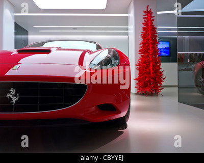 Ferrari rouge 'California' sur l'affichage de voiture de sport en vente en salle d'exposition avec l'arbre de Noël rouge derrière Banque D'Images