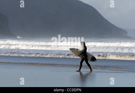 Un surfeur marche de la mer avec sa planche de surf sous le bras à Porthtowan beach, Cornwall Banque D'Images
