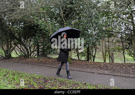 Jeune femme avec un grand parapluie noir dans un parc Brighton par temps humide, UK Banque D'Images