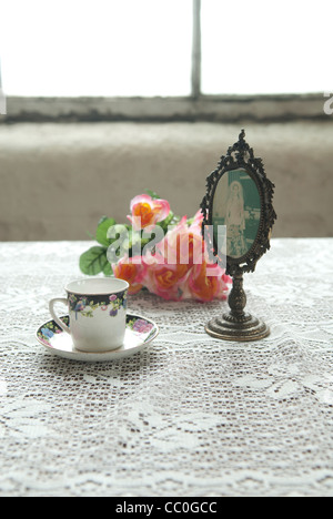 Vintage tasse de thé avec une image encadrée et roses sur une table près de la fenêtre Banque D'Images