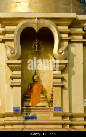 Statue de Bouddha en or avec châle drapé sur elle dans le renfoncement du stupa dans un temple bouddhiste dans le nord de la Thaïlande Banque D'Images