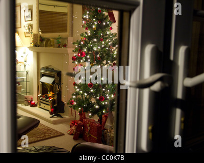 Un arbre de Noël et présente dans une chambre, vue de l'extérieur à travers une fenêtre. Banque D'Images