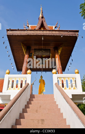 Escalier mène à l'or statue de Bouddha avec châle drapé sur elle et grosse cloche au-dessus de lui au temple bouddhiste dans le nord de la Thaïlande Banque D'Images