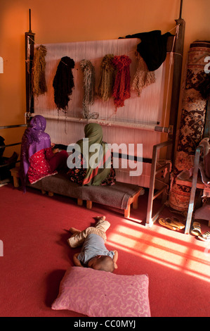 La prison de femmes de Herat - atelier de tissage - deux femmes qui travaillent et un bébé couché sur le plancher Banque D'Images